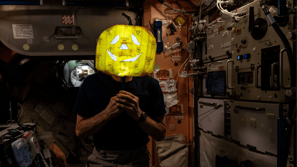 Pictured here, a crew member from Expedition 72 can be seen showing off a homemade Halloween headpiece while seated in Node 1.