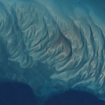 The clear blue waters off the coast of the Bahamian island of Eleuthera—part of which is visible at lower right—reveal sandbars and submerged dunes rippling across the seafloor shaped by currents and waves in the western Atlantic.