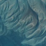The clear blue waters off the coast of the Bahamian island of Eleuthera—part of which is visible at lower right—reveal sandbars and submerged dunes rippling across the seafloor shaped by currents and waves in the western Atlantic.