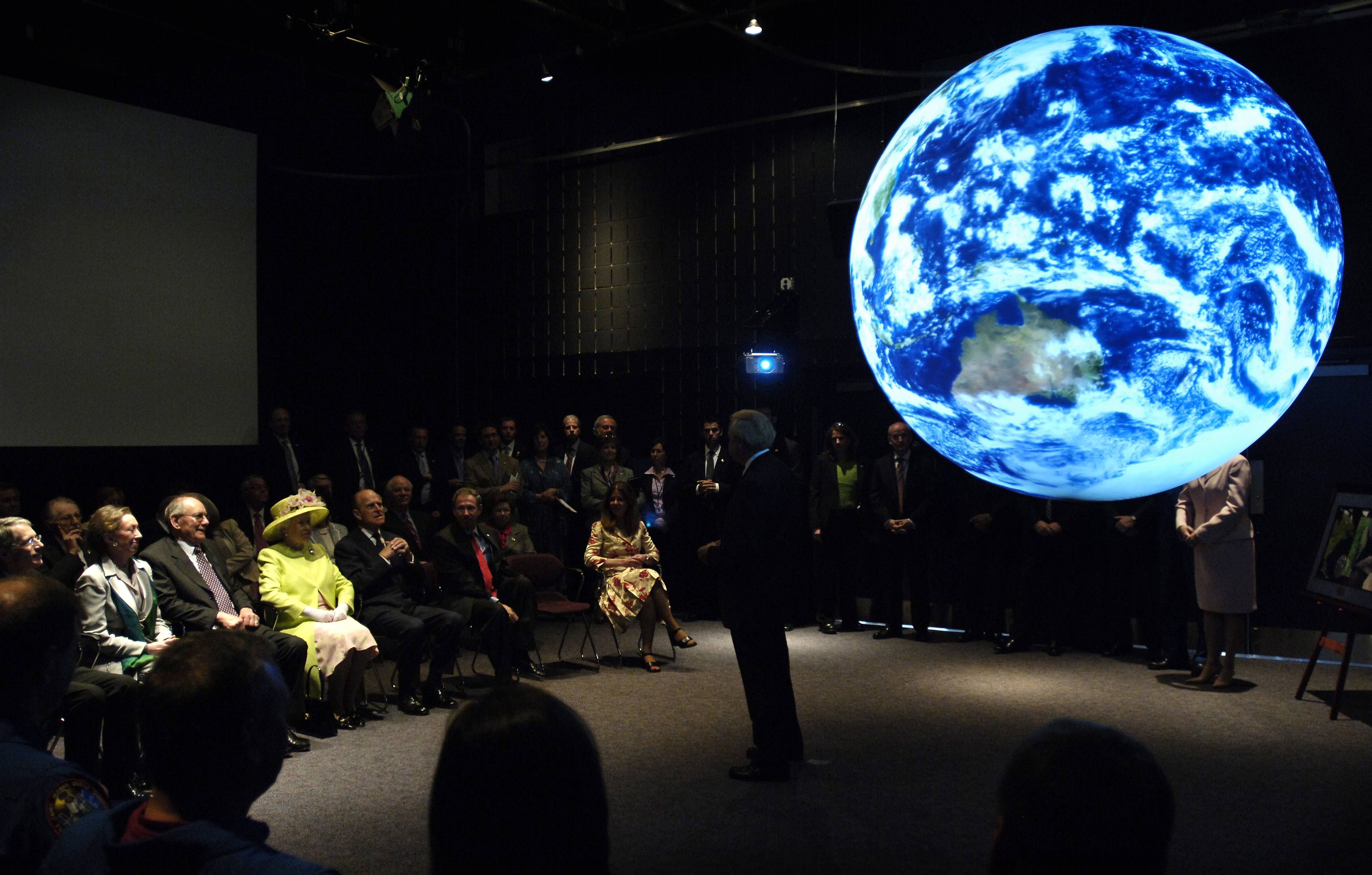 seated crowd in darkened room views illuminated Earth sphere