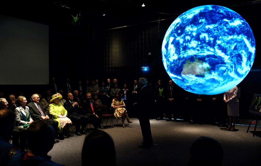seated crowd in darkened room views illuminated Earth sphere