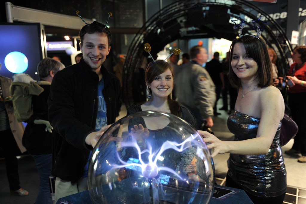 three people smile with their hands on a glass sphere with plasma streamers inside