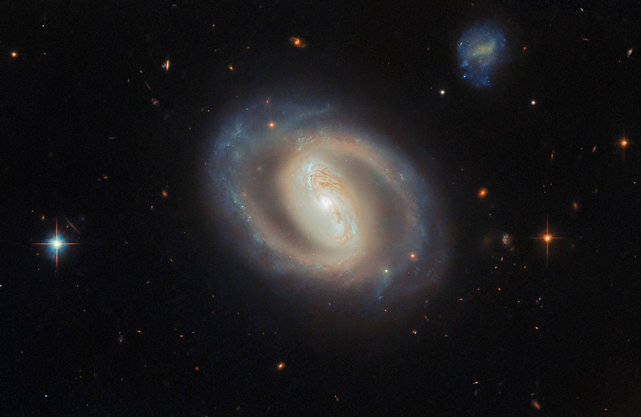 A face-on view of the barred spiral galaxy IC 486, showing a bright, elongated central bar and softly curving, ring-like spiral arms with subtle blue star-forming regions and dark dust lanes, set against a black background dotted with distant galaxies and a few foreground stars.