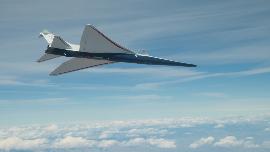 NASA's X-59 supersonic jet with blue hull and white wing and tail is seen from below as it flies among clouds.