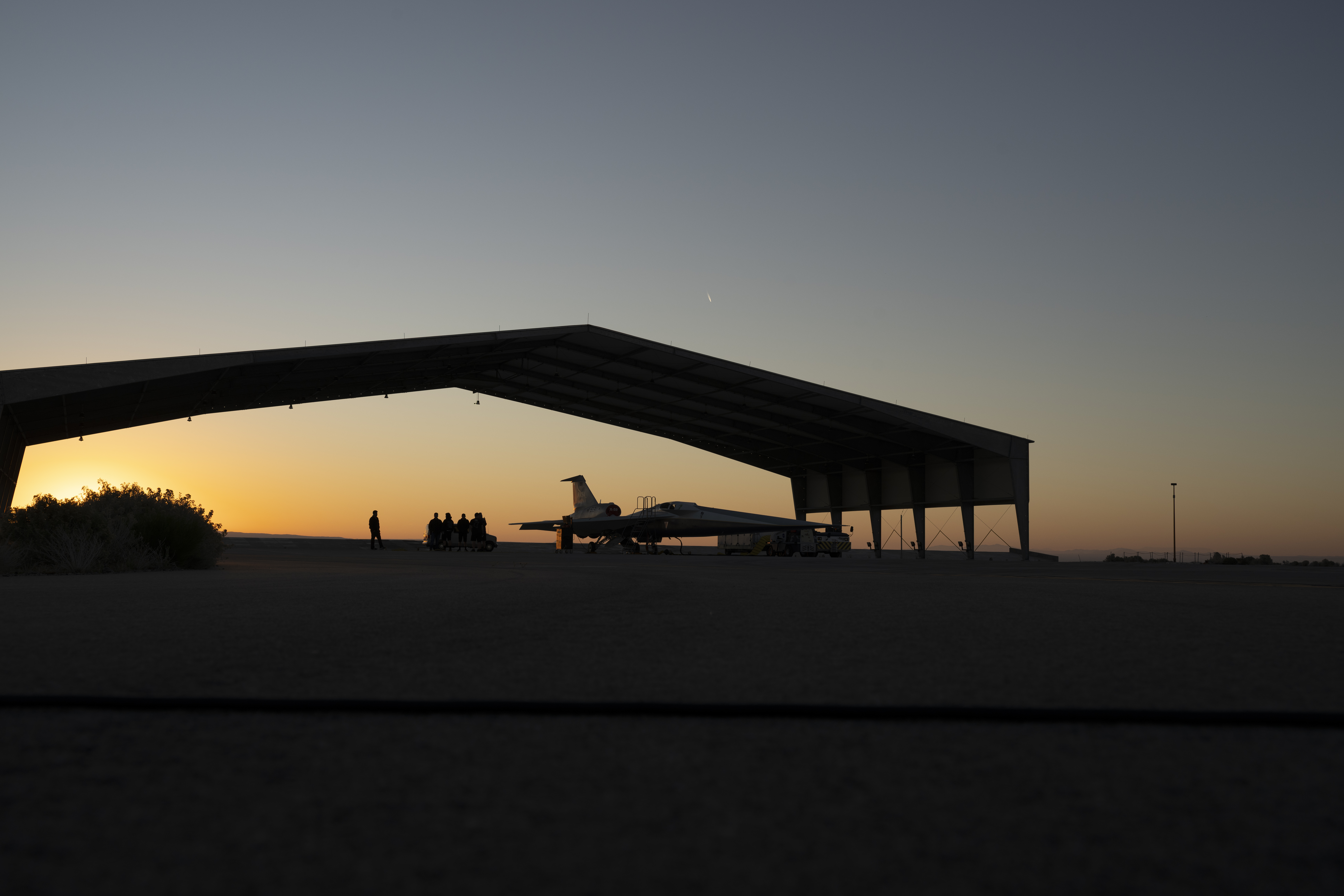 NASA's X-59 silhouetted in the foreground, parked in a run stall at sunrise.