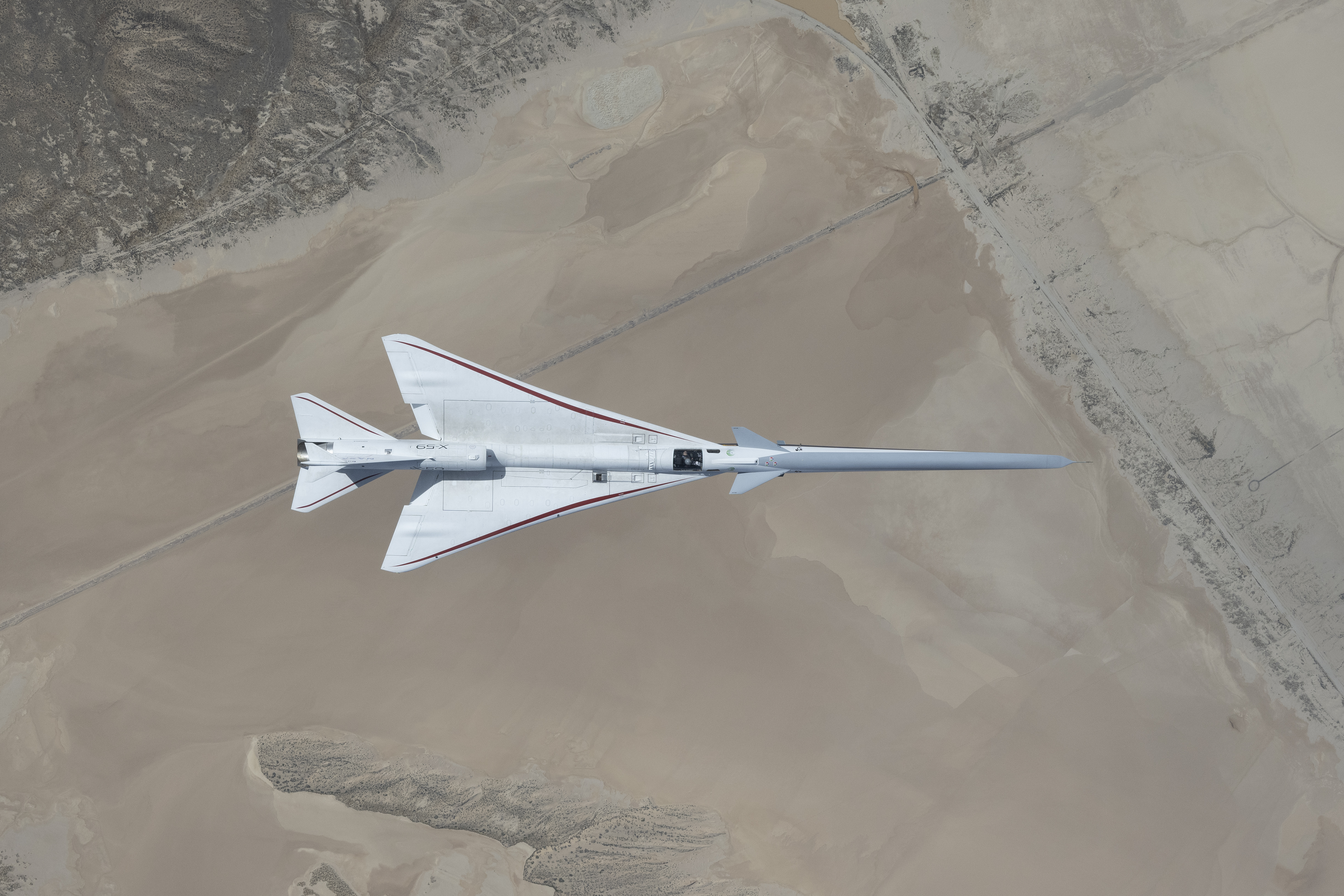 Aerial view looking down onto the X-59 while it's in flight over the Mojave Desert.