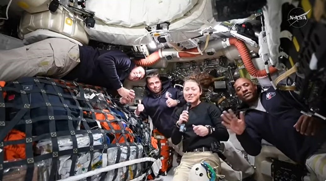 Four astronauts float amongst equipment and supplies inside the Orion spacecraft.