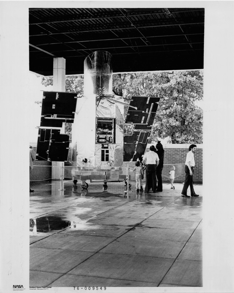 black-and-white photo of a large cylindrical satellite with two solar panel wings