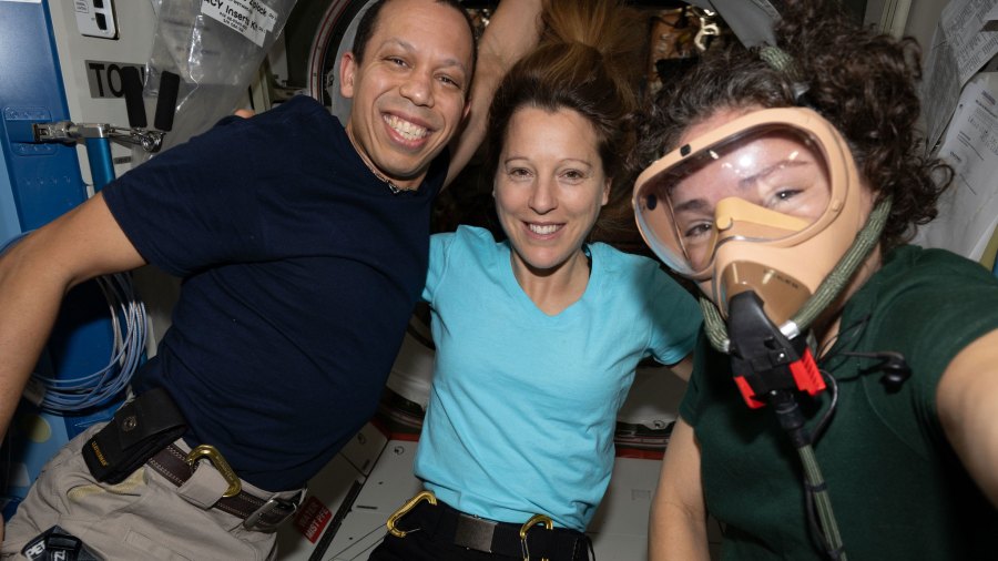 Expedition 74 flight engineers (from left) Chris Williams of NASA, Sophie Adenot of ESA (European Space Agency), and Jessica Meir of NASA pose for a portrait aboard the International Space Station. Meir is wearing a portable breathing apparatus to test its readiness for unlikely emergency scenarios such as an oxygen leak, chemical leak, or fire aboard the orbital outpost.