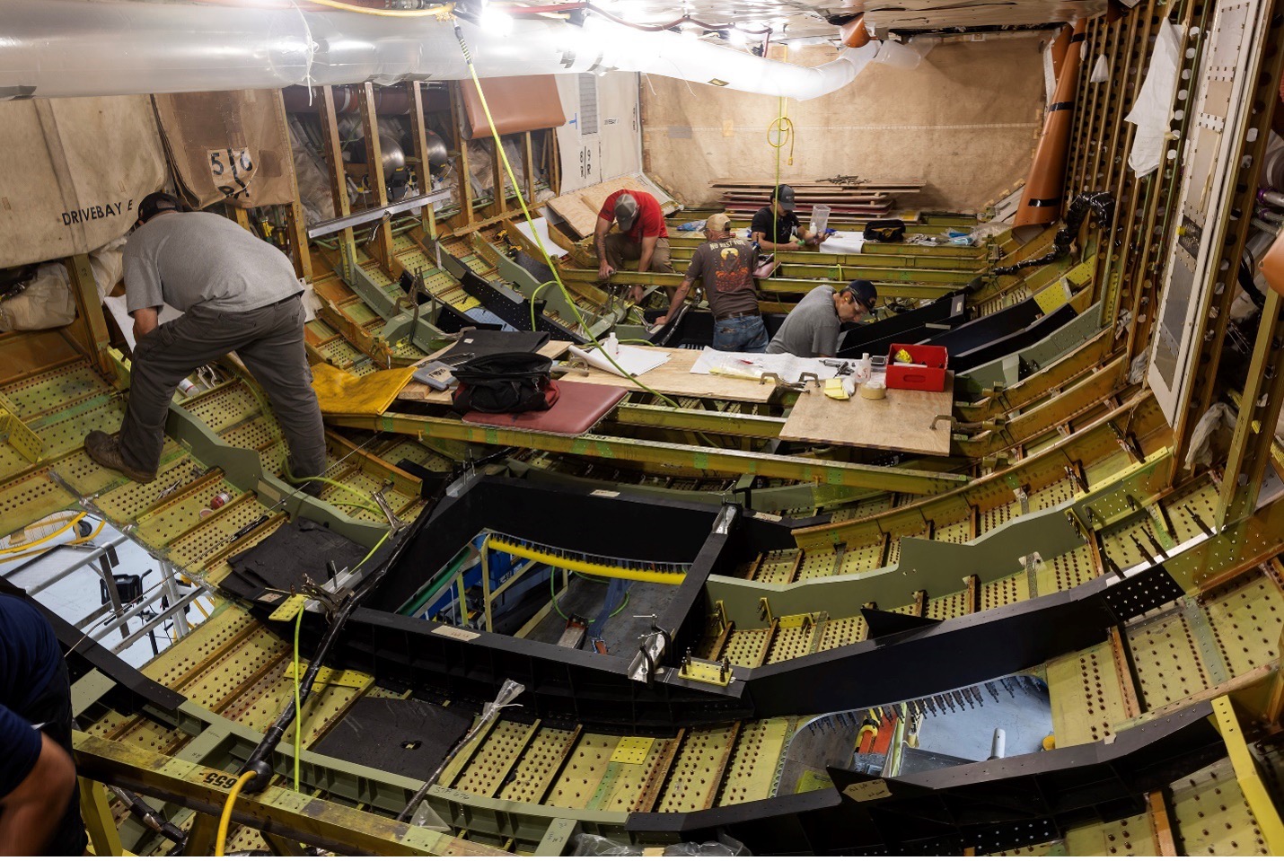 A view from inside the cabin of the 777 shows holes in the bottom of the fuselage where viewports have been cut. Workers are throughout the cabin, standing above and below the ports.