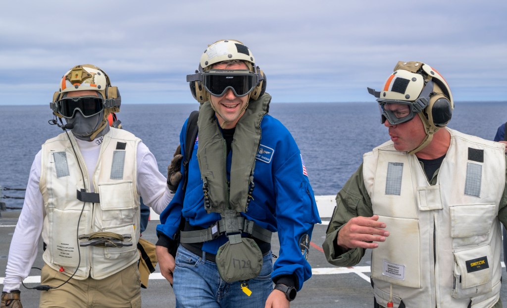 NASA Administrator Jared Isaacman, center, is greeted by Capt. Erik Kenny, commanding officer, USS John P. Murtha (LPD), right, after...