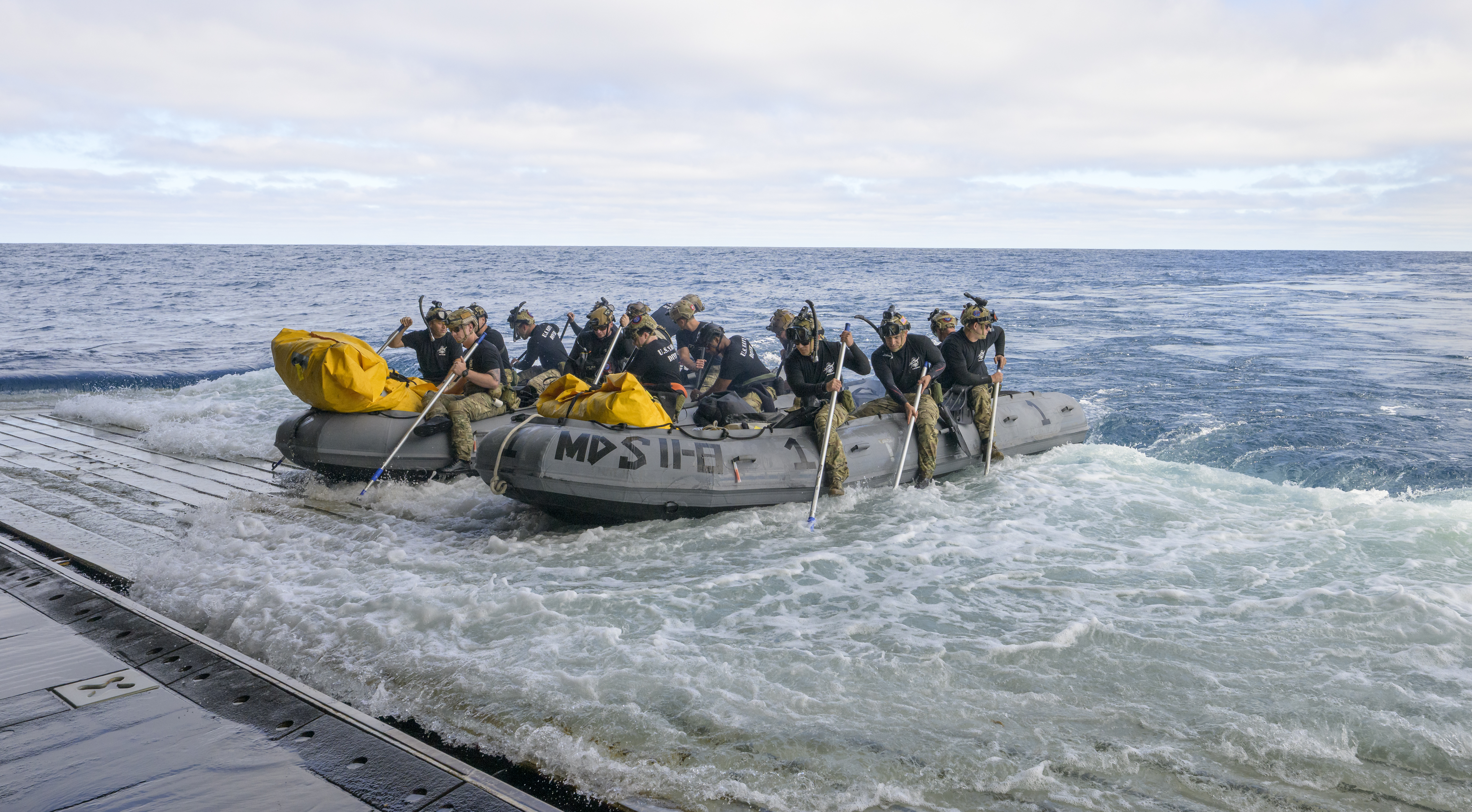 U.S. Navy divers prepare to deploy in small boats from the well deck of USS John P. Murtha to recover...
