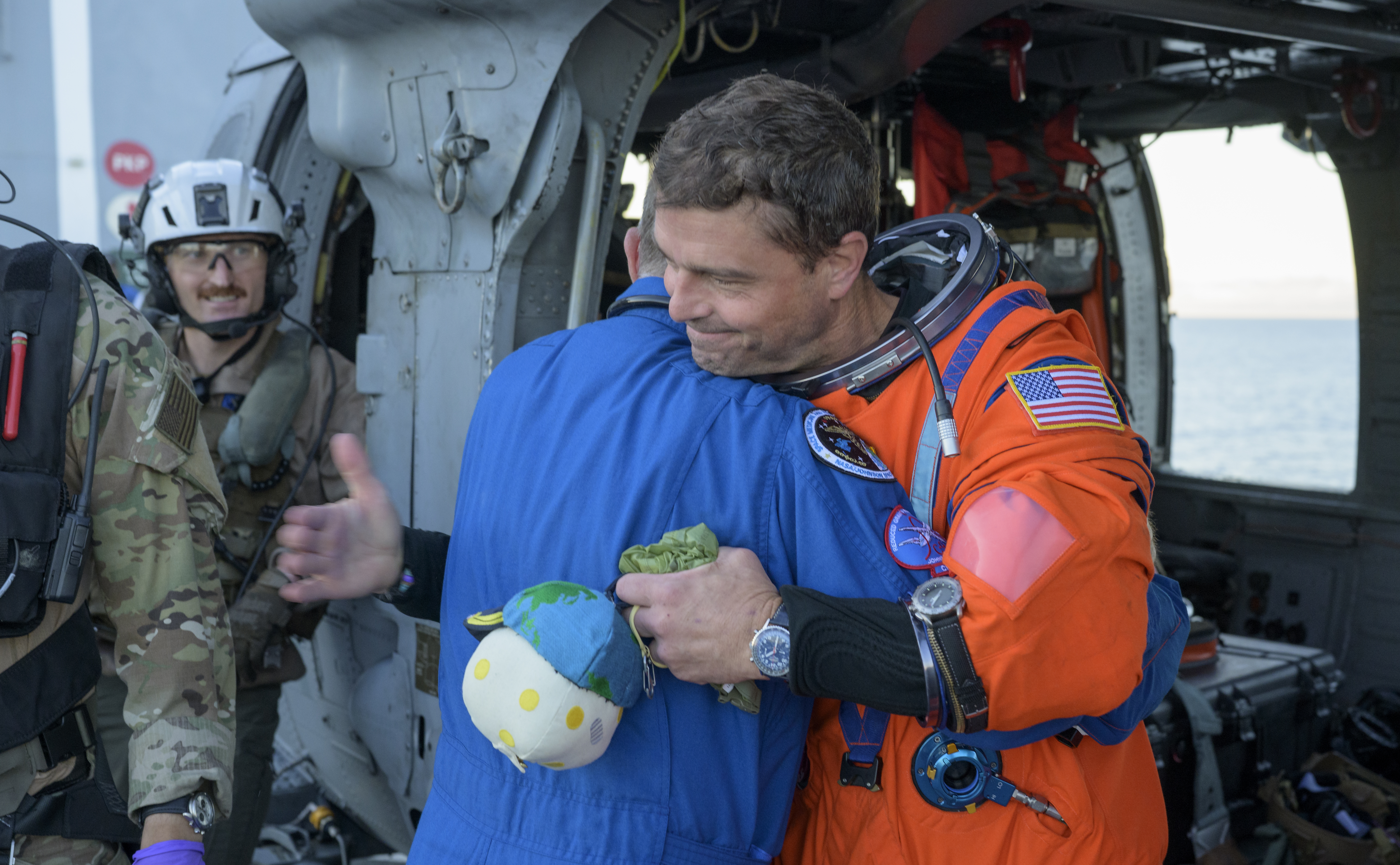 NASA astronaut Reid Wiseman, Artemis II commander, gives NASA Flight Surgeon Richard Scheuring a hug next to a Navy MH-60...