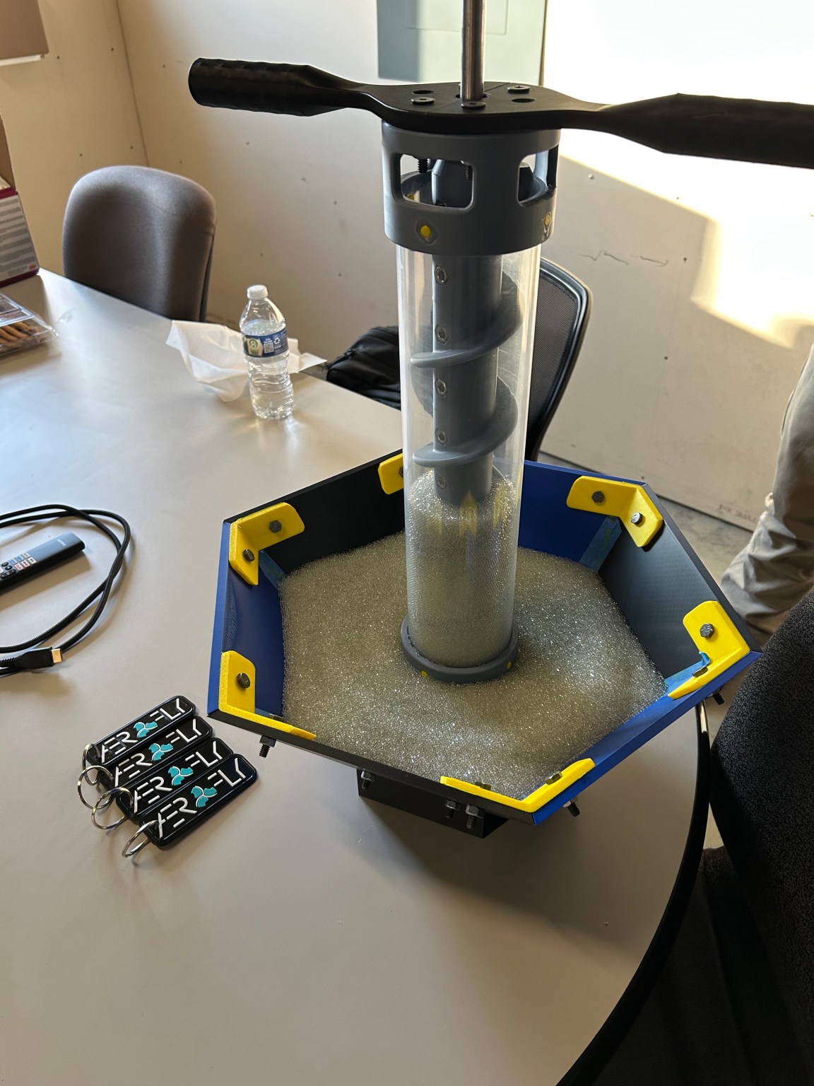 A tall clear cylinder containing sand and an auger sits in a dish on a countertop.
