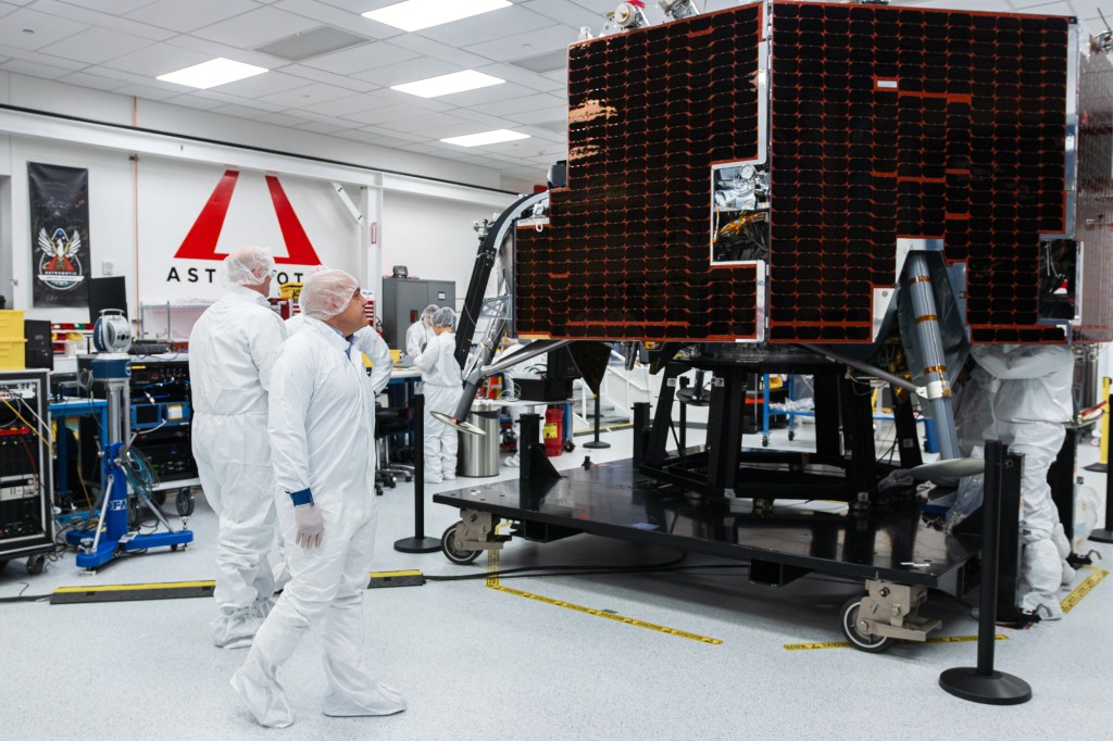 NASA Moon Base program leaders walk around Astrobotic’s Griffin-1 lunar lander inside a clean room in Pittsburgh, Pennsylvania. Large dark solar panels covers the side of the spacecraft as engineers work nearby in the background.
