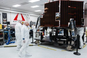 NASA Moon Base program leaders walk around Astrobotic’s Griffin-1 lunar lander inside a clean room in Pittsburgh, Pennsylvania. Large dark solar panels covers the side of the spacecraft as engineers work nearby in the background.