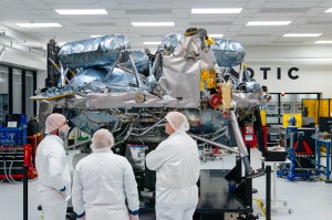 Three people stand in front of Astrobotic’s Griffin-1 lunar lander inside a clean room in Pittsburgh, Pennsylvania. The large lunar lander dominates the foreground as the group views the spacecraft.