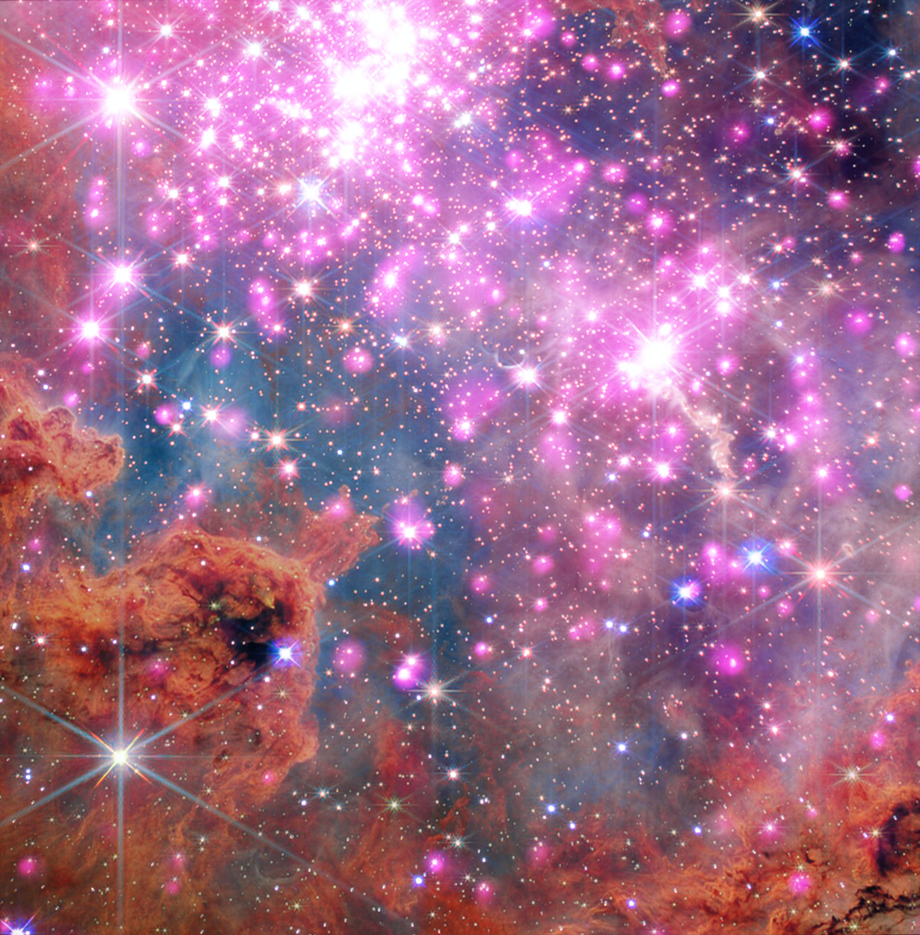 Scores of gleaming stars ringed in neon pink stretch across the frame, highlighting a cluster where stars are between one and three million years old. Brick-orange dust clouds along the bottom edge illustrate the raw materials of this active stellar nursery.