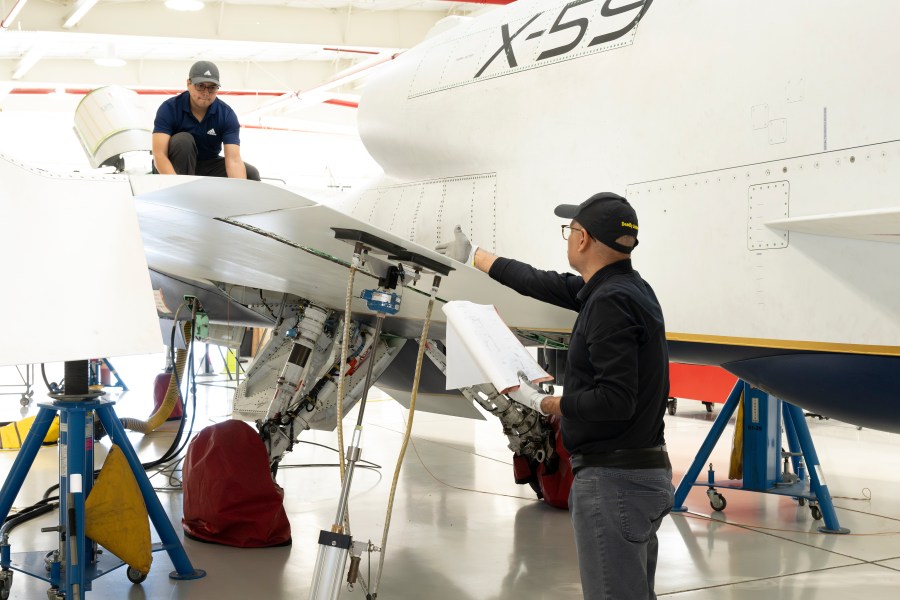 Workers examine the wing area of the X‑59 aircraft inside a hangar.