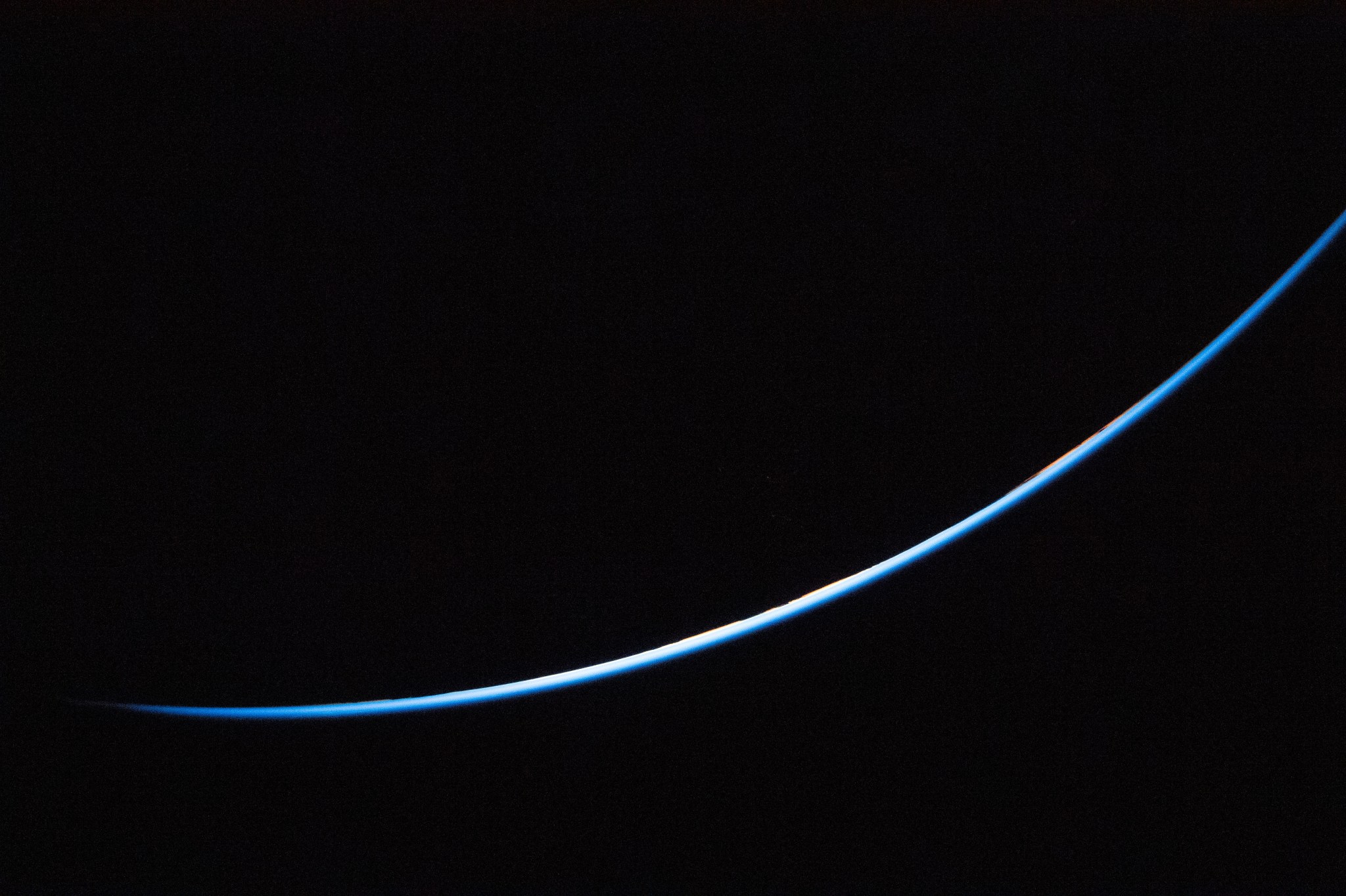 The edge of Earth is a thin line curving upward from left to right. The line is different shades of blue.
