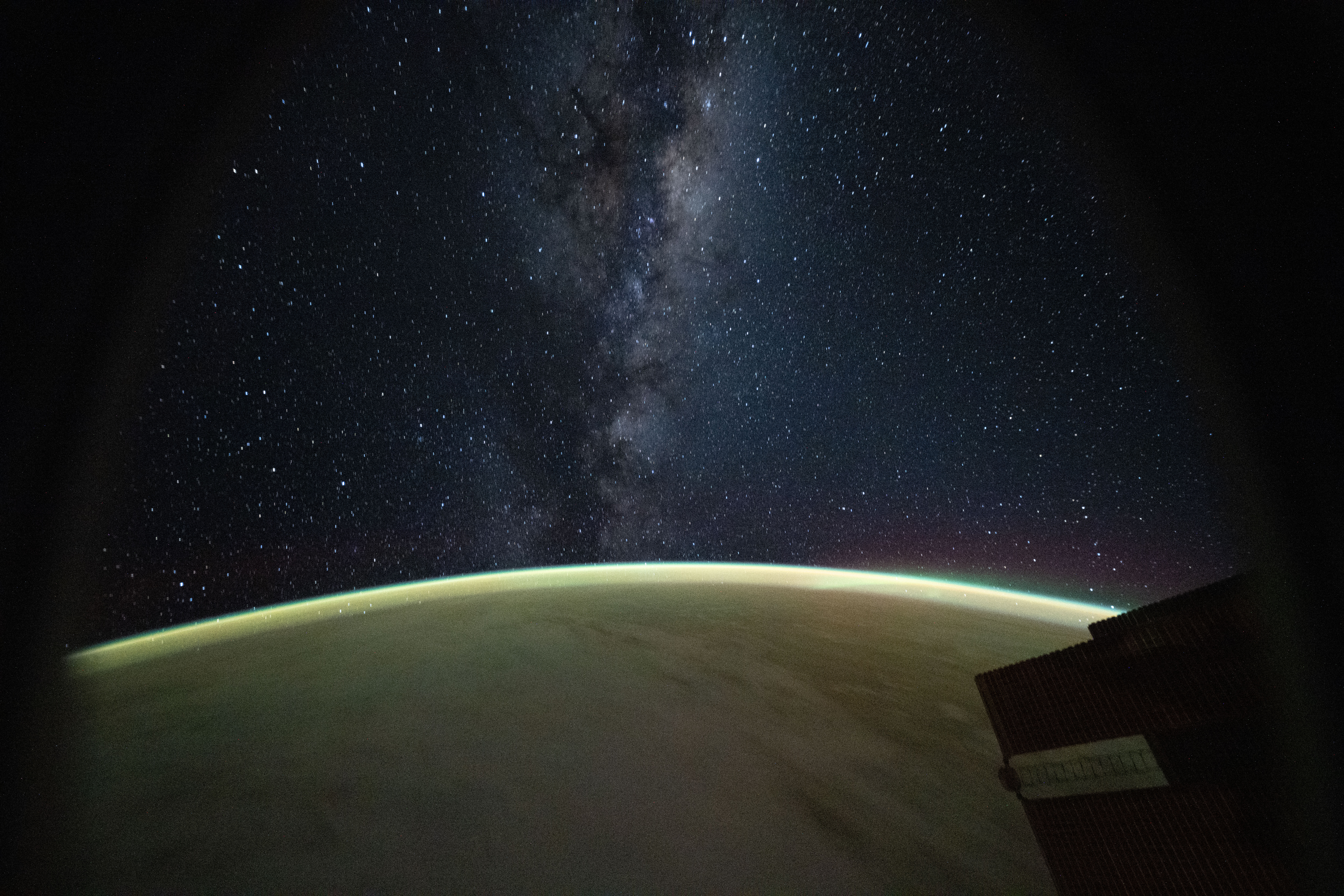 The Milky Way galaxy appears above Earth's greenish atmospheric glow. The galaxy's dust and stars can be seen against the darkness of space.
