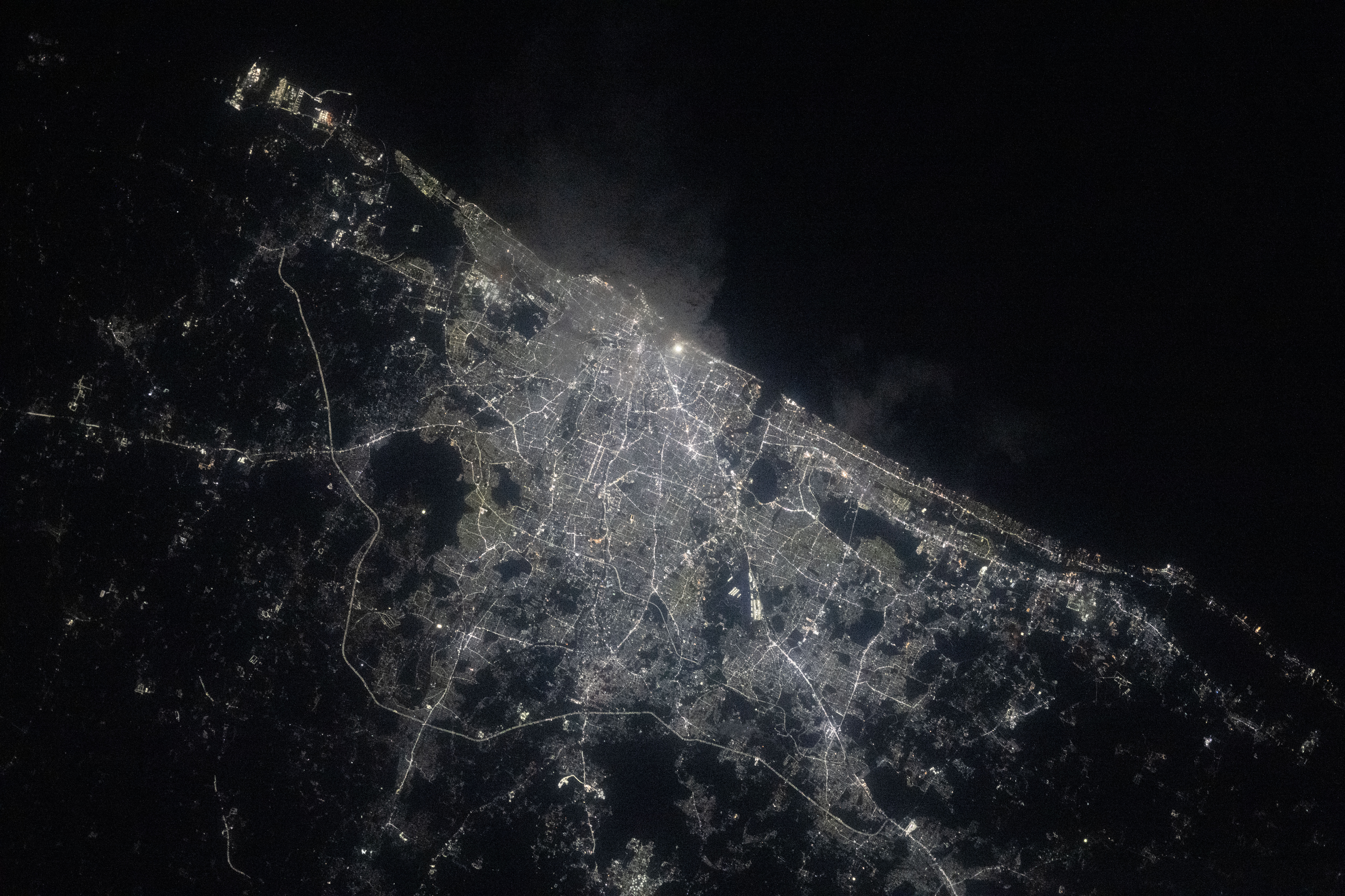 A view of Chennai at night from the International Space Station shows a sprawling city along the water (upper right). City lights make the city shine while also highlighting roadways. The surrounding area is mostly dark.