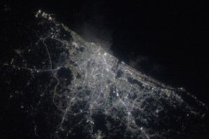 A view of Chennai at night from the International Space Station shows a sprawling city along the water (upper right). City lights make the city shine while also highlighting roadways. The surrounding area is mostly dark.