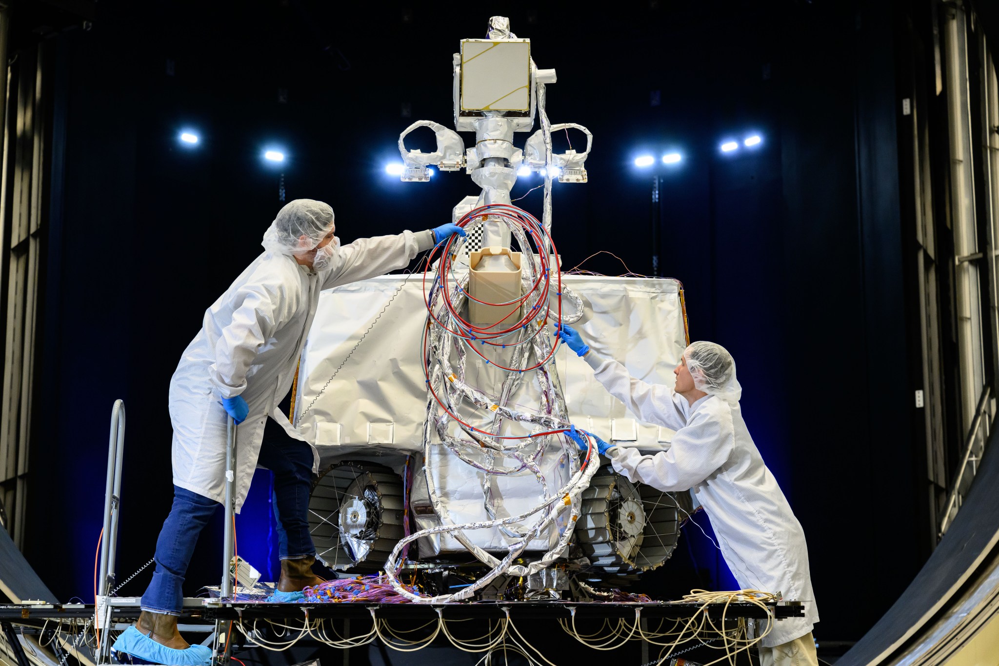 Two technicians in clean room attire work on NASA’s VIPER (Volatiles Investigating Polar Exploration Rover) during testing inside a chamber at NASA’s Johnson Space Center in August 2024.