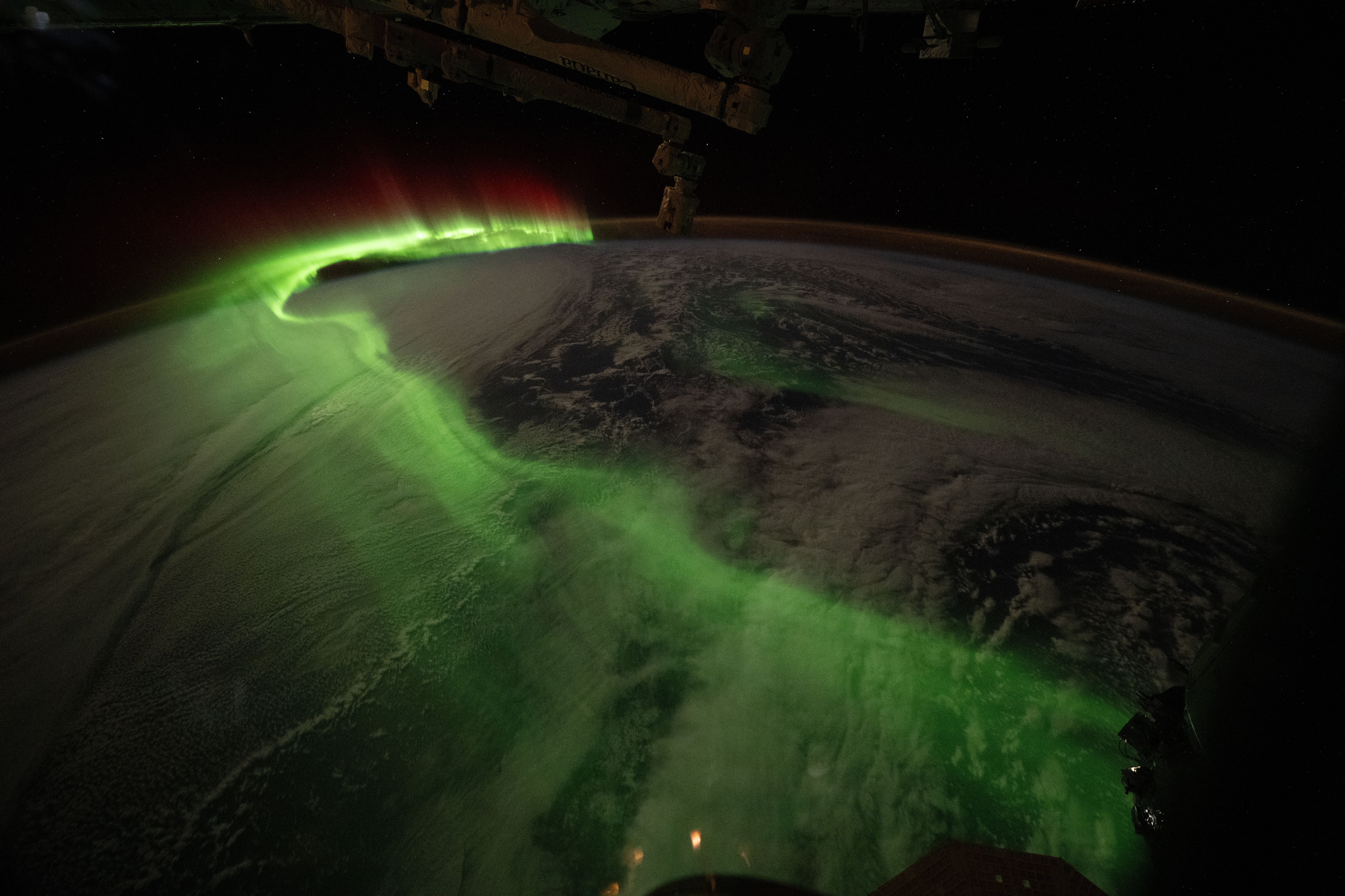 The aurora looks like a long, curving line of green mist arcing over Earth. Our home planet is dark, blending into the blackness of space on the right side of the image.