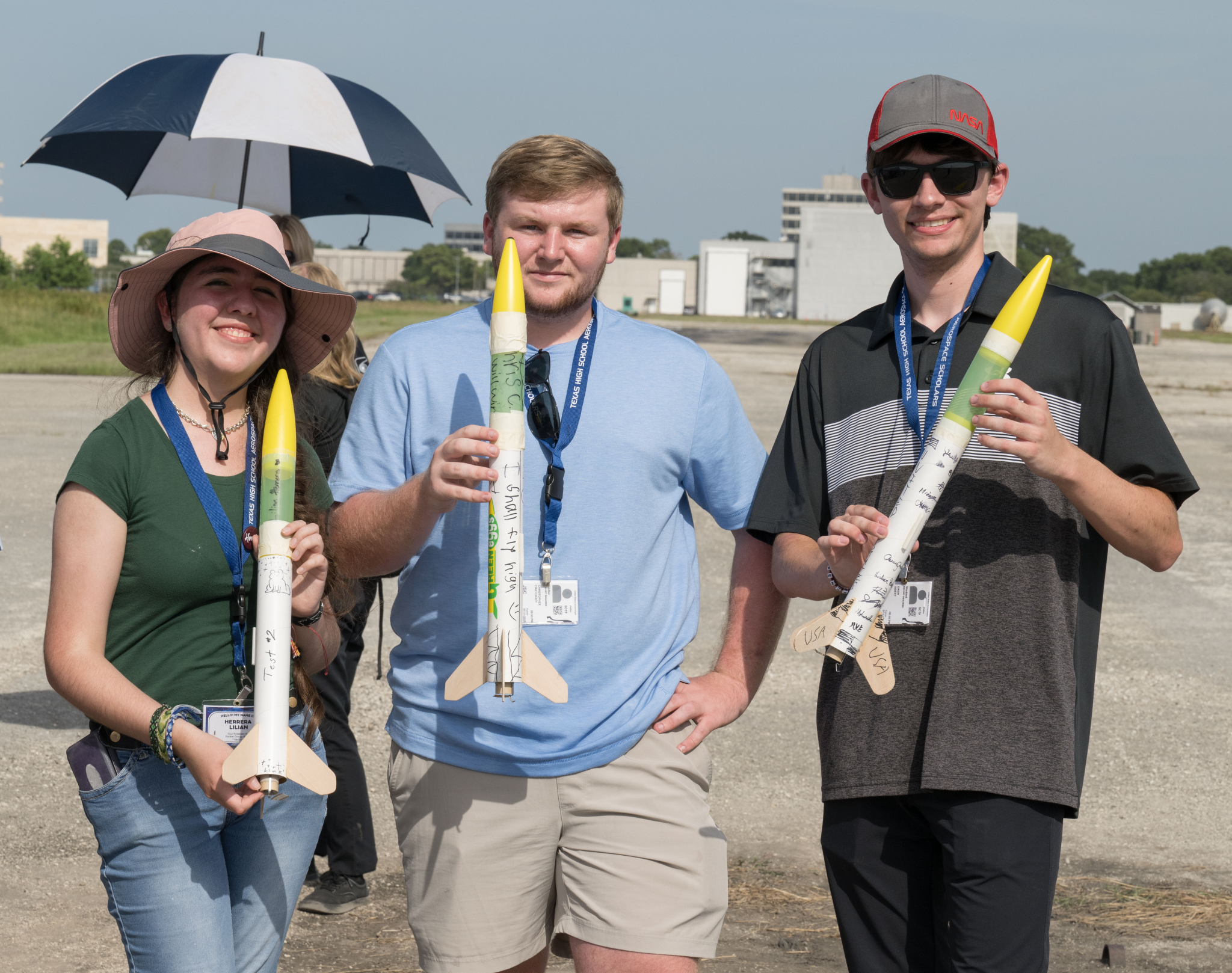 3 students holding model rockets smile at the camera