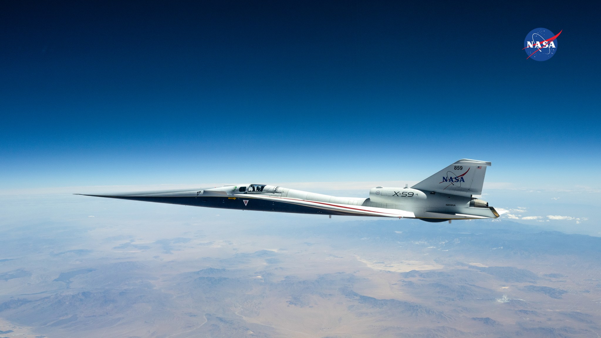 NASA’s X‑59 flies at high altitude under a dark blue sky above the desert landscape.