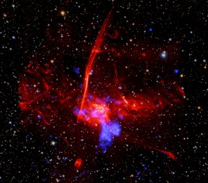 Set against a backdrop packed with distant stars and other specks of light are two distinct, overlapping clouds. The larger, visually dominant cloud, is red and multifaceted. It has an irregular shape, and features patches of different textures, including pockets that resemble wispy smoke, tangles of faint red veins, and clear streaking lines. This large cloud of expanding gas represents radio data from the MeerKAT telescope in South Africa. Overlapping with that red cloud is a cloudy blue blob representing X-ray data from NASA's Chandra X-ray Observatory and ESA's XMM-Newton.