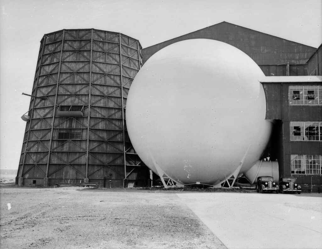 A dark, silo-shaped building to the left of a white building shaped like a sphere.
