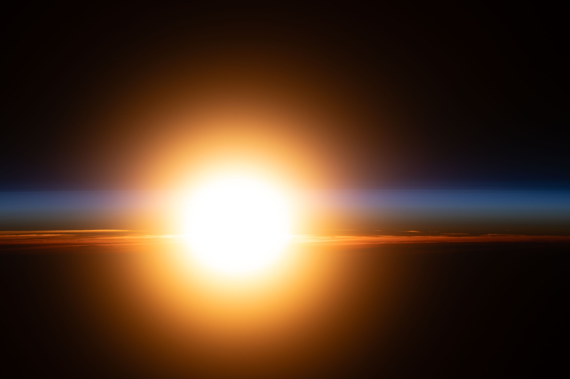 A bright orange sunburst illuminates Earth's atmosphere during an orbital sunrise.