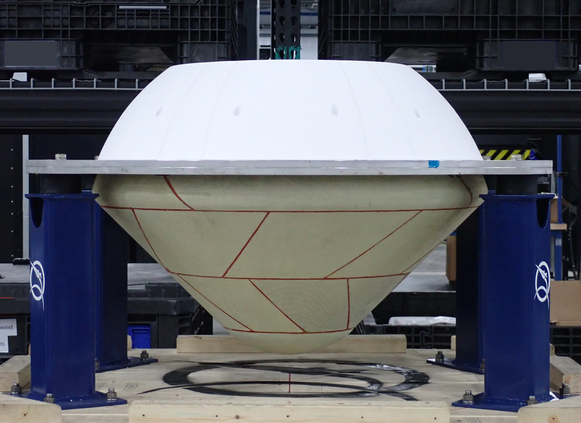 A diagonally segmented, cone-shaped capsule with a white domed and flattened top sits in a warehouse.