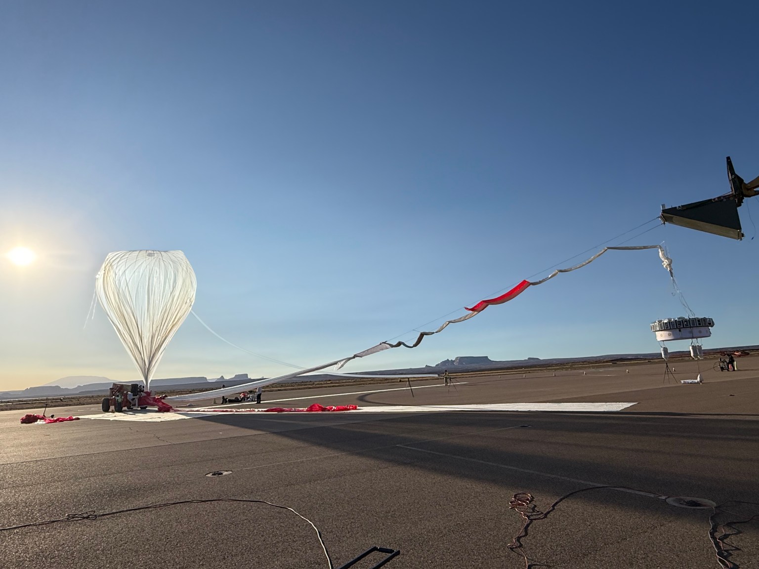 A high-altitude balloon tethered to a gondola of experiments sits on the tarmac.