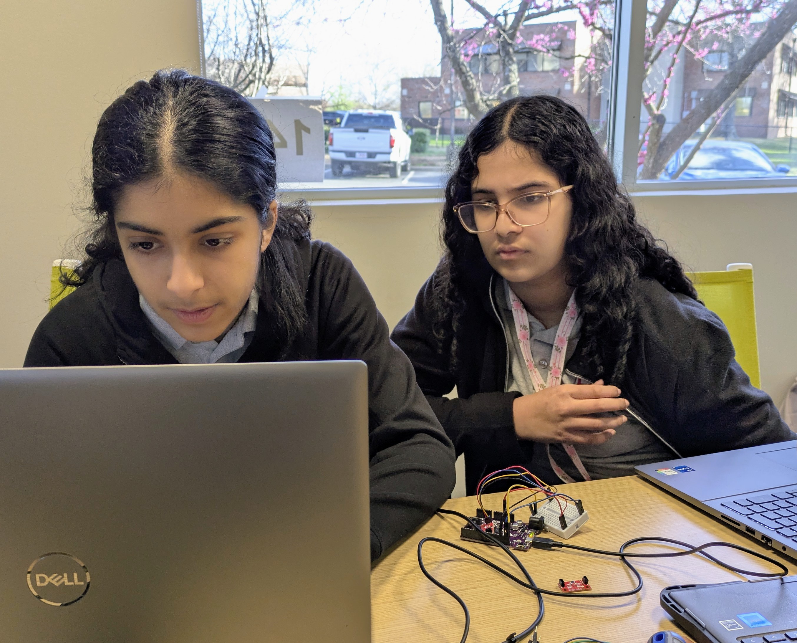 Two students look at a laptop screen with a wired device sitting in front of them.