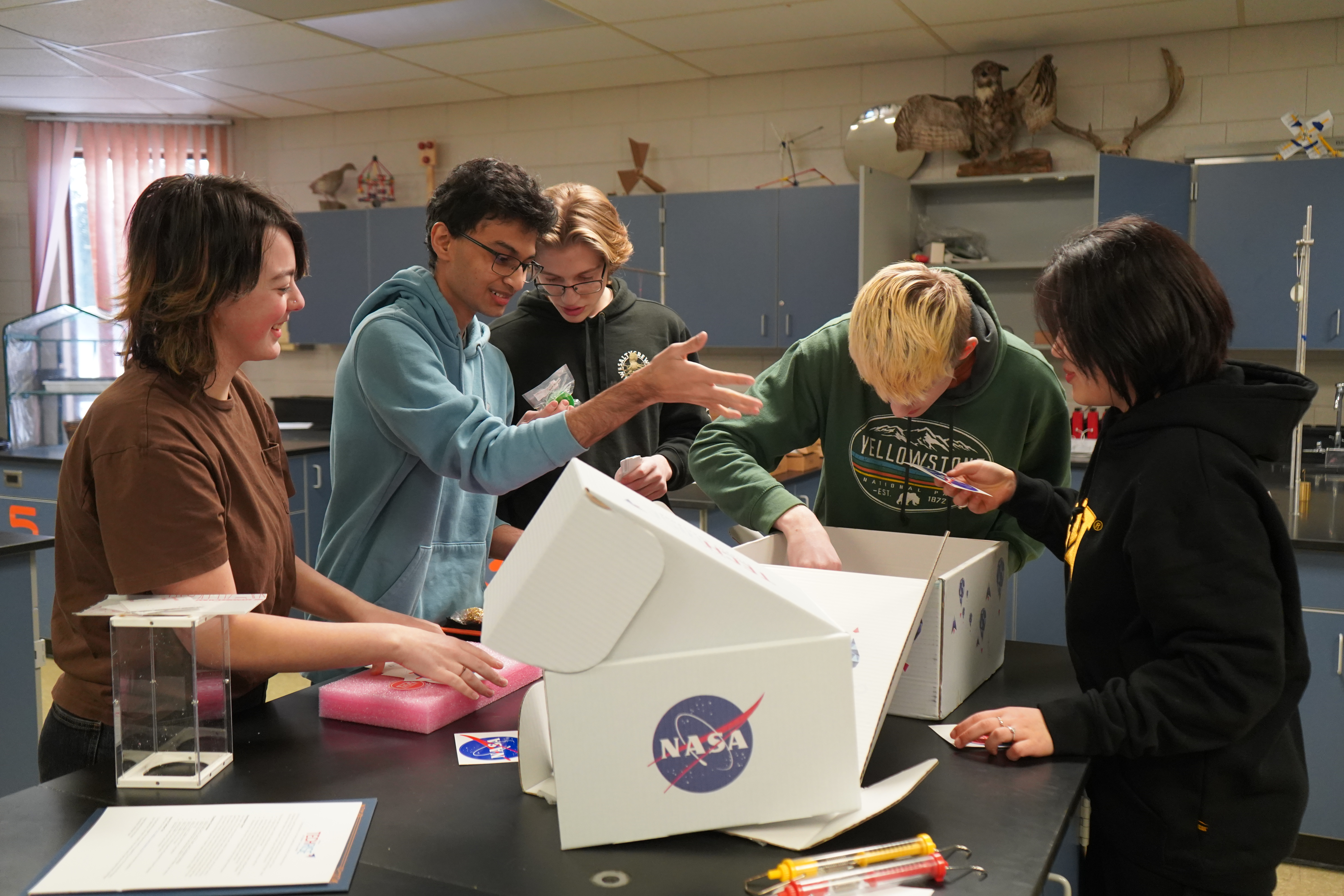 Five students unpack white boxes with NASA logos.