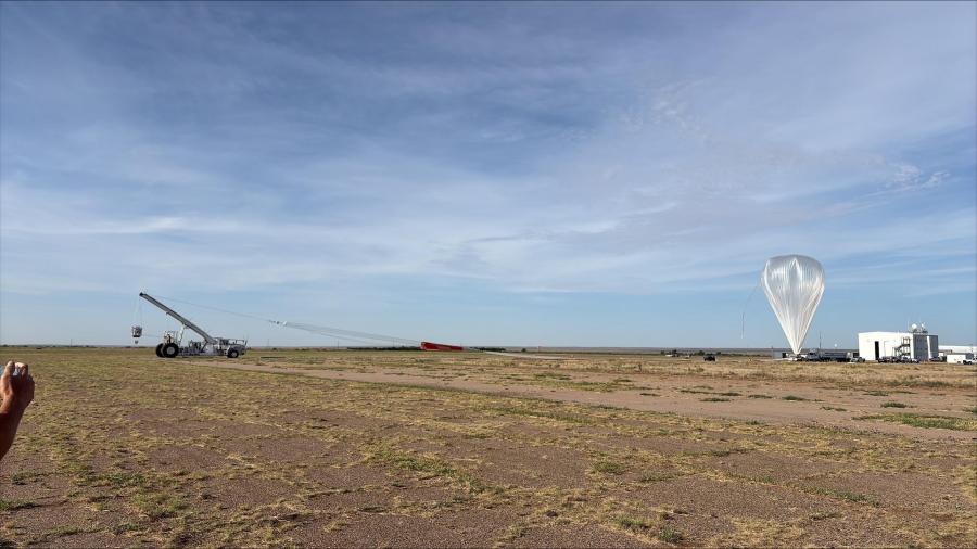 A scientific balloon is partially inflated on the right with the mobile launch vehicle carrying a payload on the left.