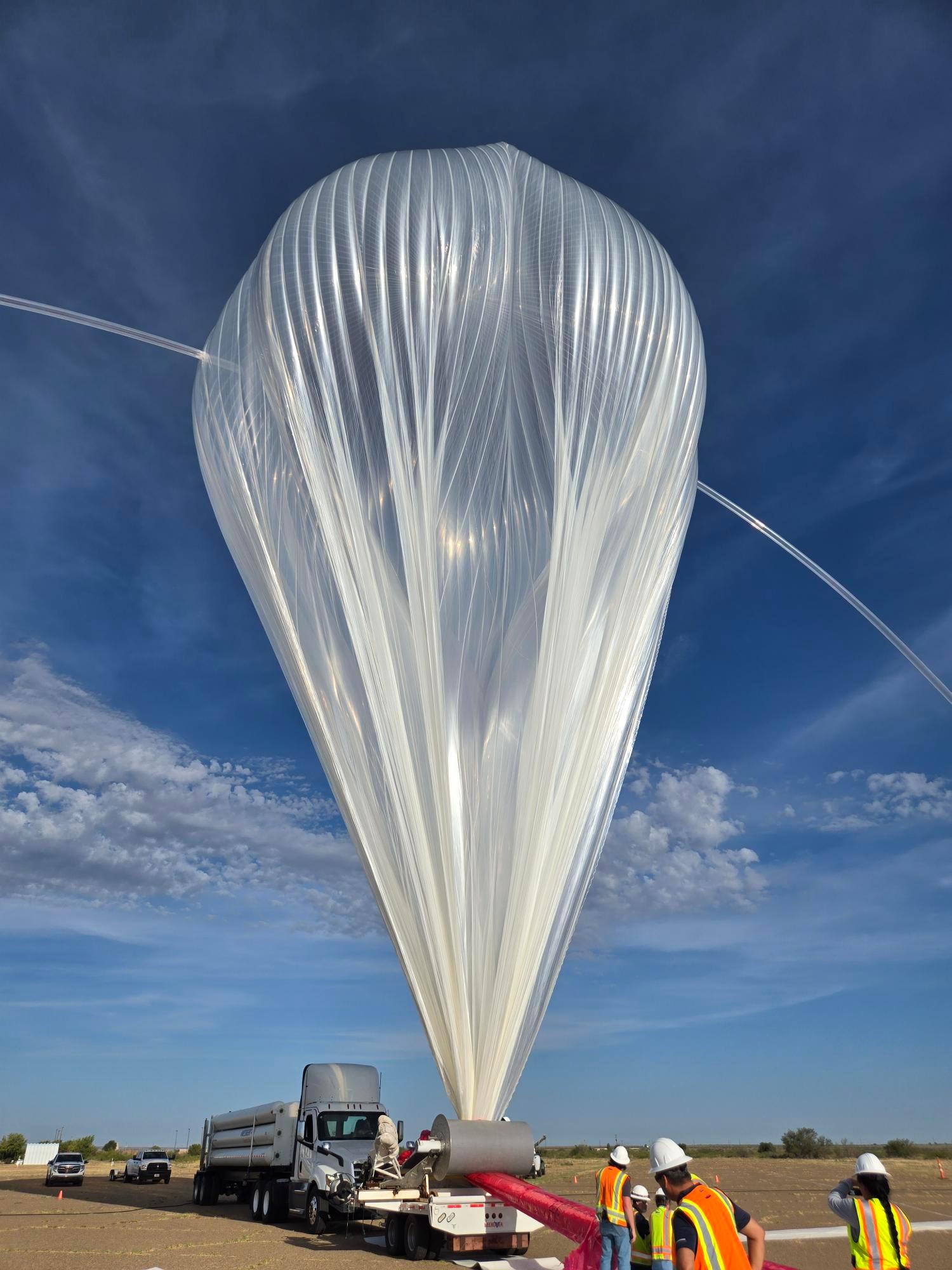 A scientific balloon partially inflated against a a blue partially cloudy sky.