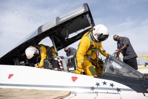 Two people in slim yellow spacesuits and white helmets climb into an airplane as technicians work around them.