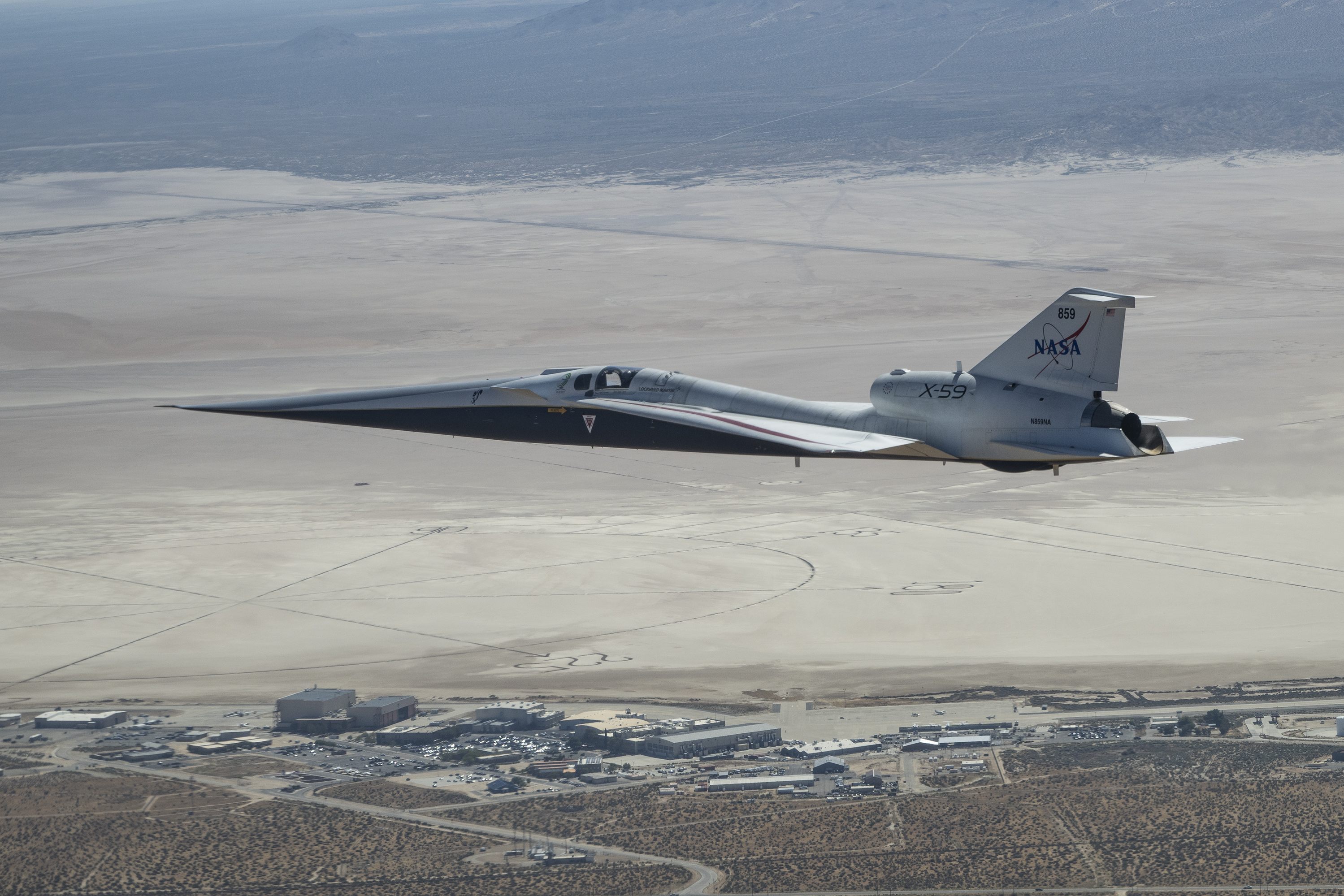 NASA’s X-59 quiet supersonic research aircraft flies above NASA’s Armstrong Flight Research Center and Rogers Dry Lake in California. The aircraft is shown in side profile during level flight with the compass rose, facilities, and desert terrain below.