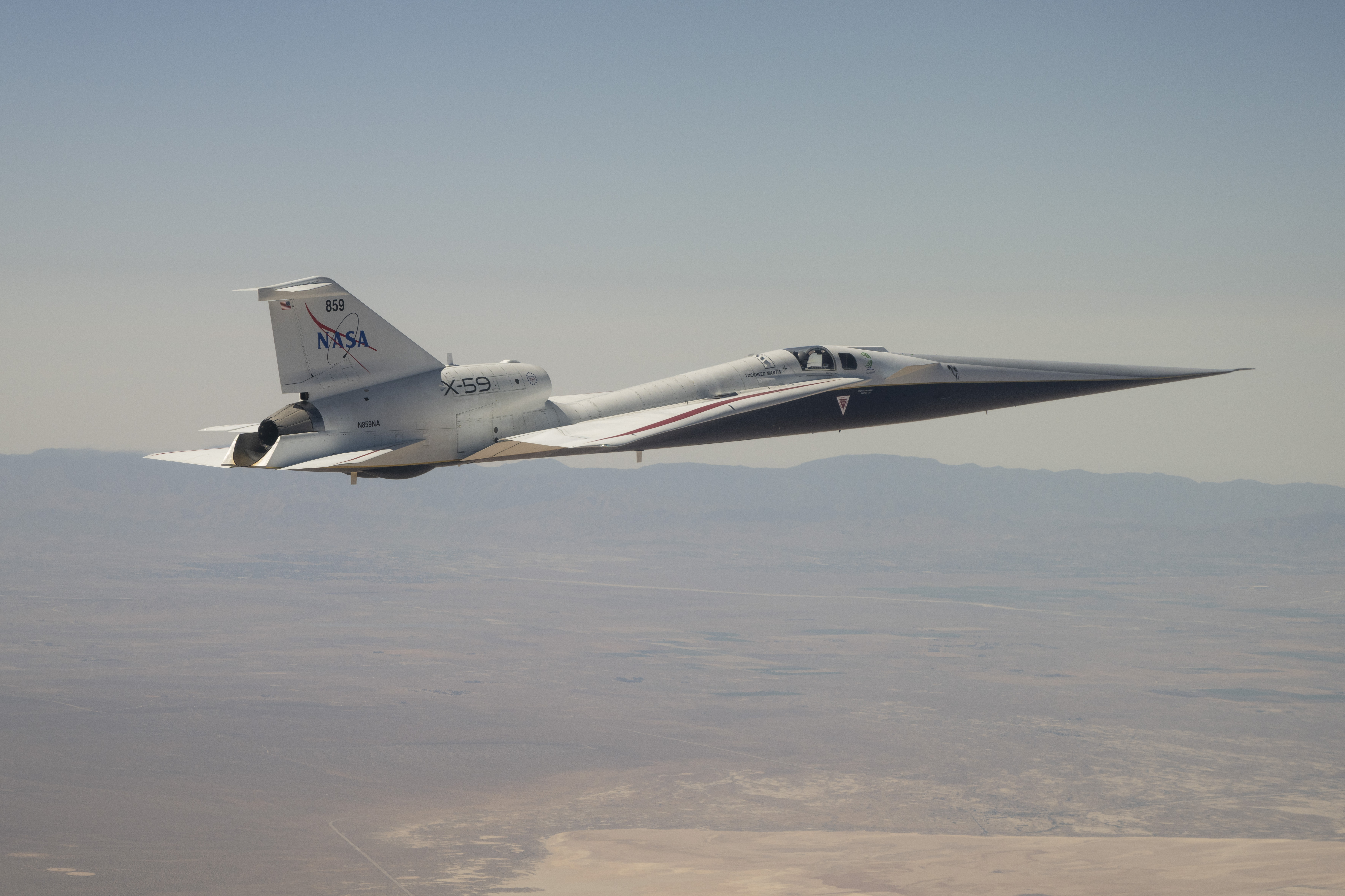 NASA’s X-59 quiet supersonic research aircraft is shown flying above mountain ridges in California during a test flight on May 12, 2026. The aircraft is viewed from above, showing its elongated nose, swept wings, and white fuselage against layered mountains and valleys below.
