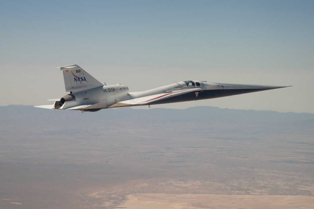 NASA’s X-59 quiet supersonic research aircraft is shown flying above mountain ridges in California during a test flight on May 12, 2026. The aircraft is viewed from above, showing its elongated nose, swept wings, and white fuselage against layered mountains and valleys below.
