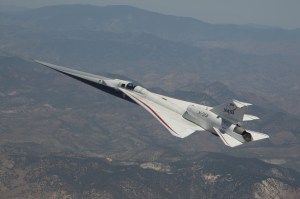 NASA’s X-59 quiet supersonic research aircraft is shown flying above mountain ridges in California during a test flight on May 12, 2026. The aircraft is viewed from above, showing its elongated nose, swept wings, and white fuselage against layered mountains and valleys below.