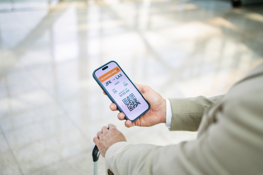 An image for the Smart Skies Crossword Puzzle showing a business man holding a cellphone showing JFK and LAX airport codes on his digital boarding pass.