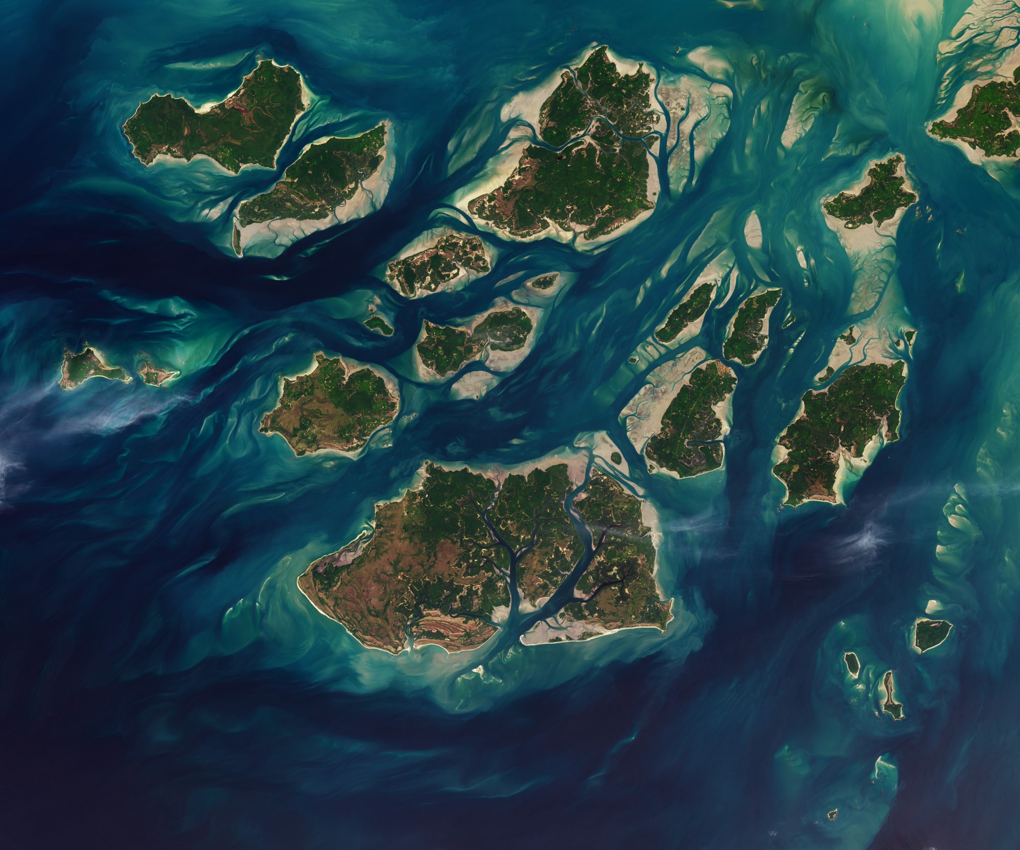A satellite image shows a cluster of green islands surrounded by beige sand flats and networks of channels full of dark blue water.