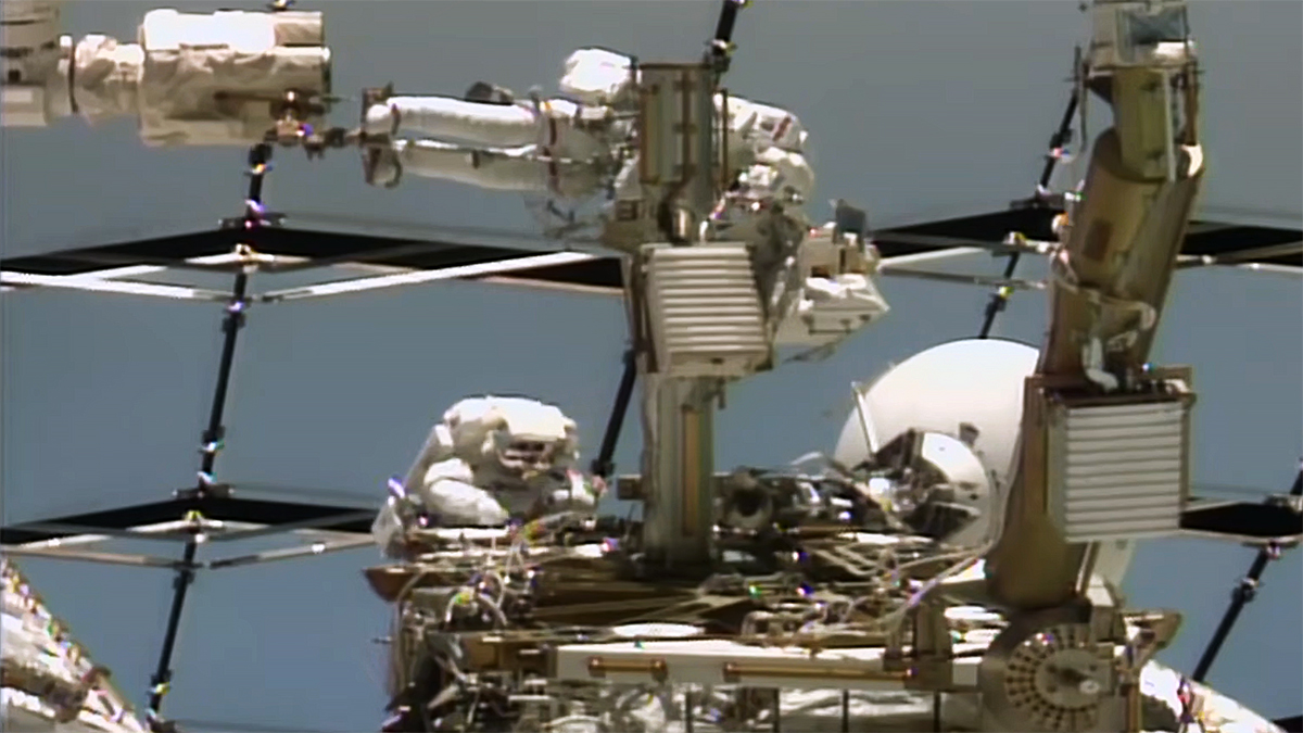 Astronauts Anil Menon of NASA (top) and Sophie Adenot of ESA (European Space Agency) work on a space-to-ground antenna outside the International Space Station.