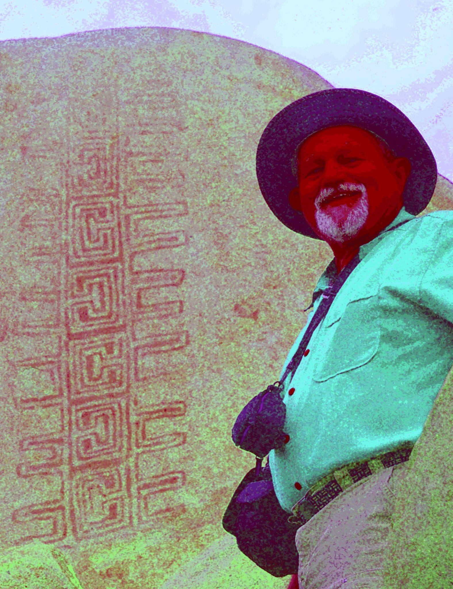 A man stands in front of a rock with art on it, the colors are intense and exaggerated revealing an intricate design in the rock's surface.