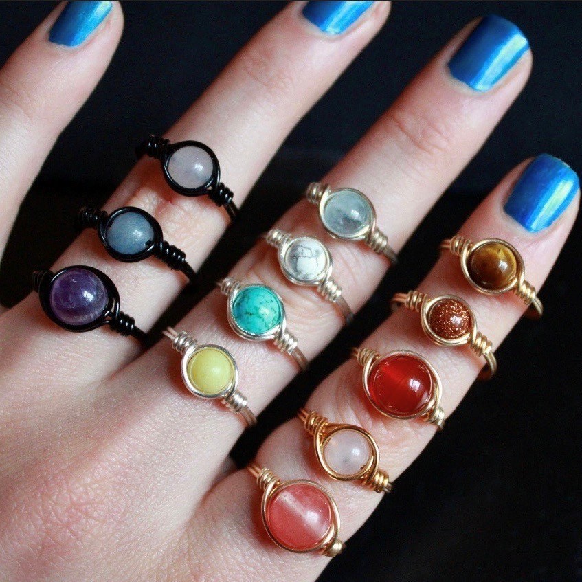 Multiple, handmade rings with stones displayed on a hand model with blue nail polish.